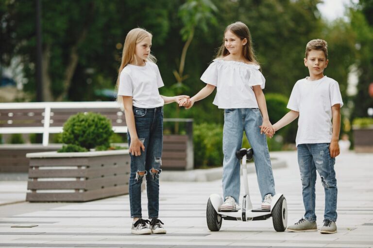 Three children holding hands, one on a segway, enjoying a playful day in an urban outdoor park.