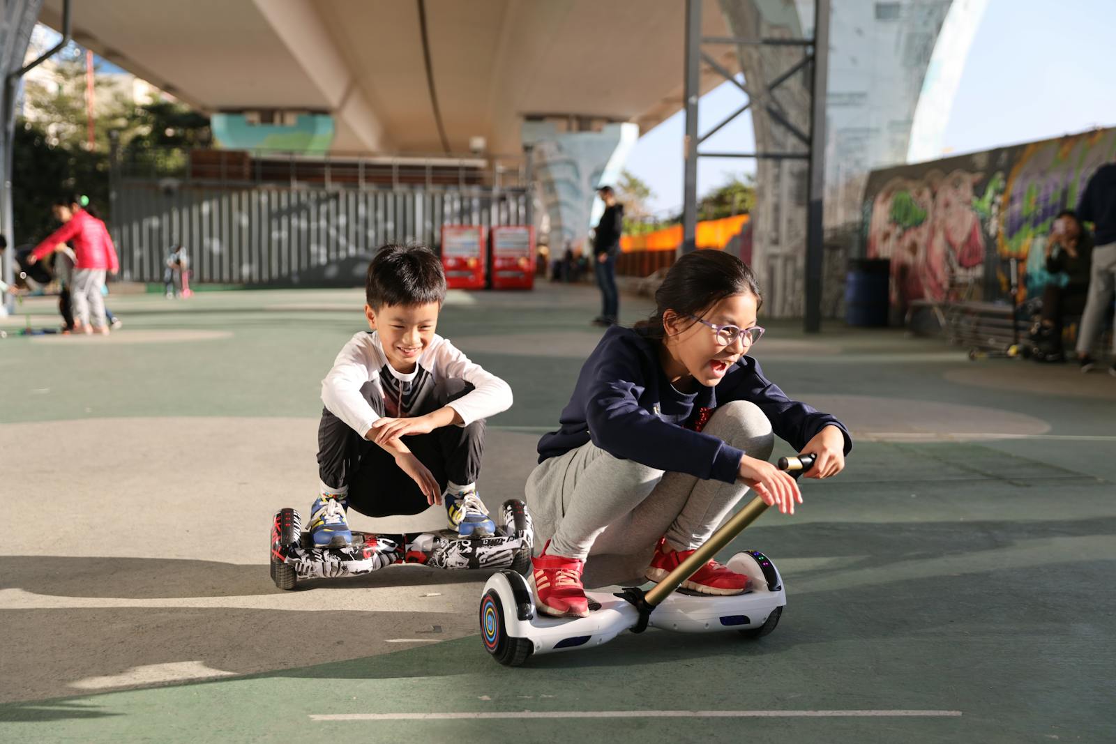 Two children having fun riding hoverboards in an urban skate park setting.