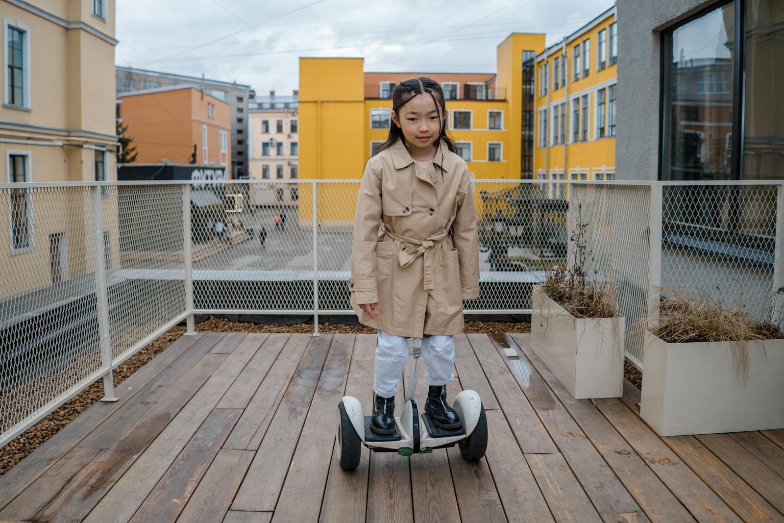 A young girl rides a hoverboard on a wooden deck outdoors, showcasing balance and fun.